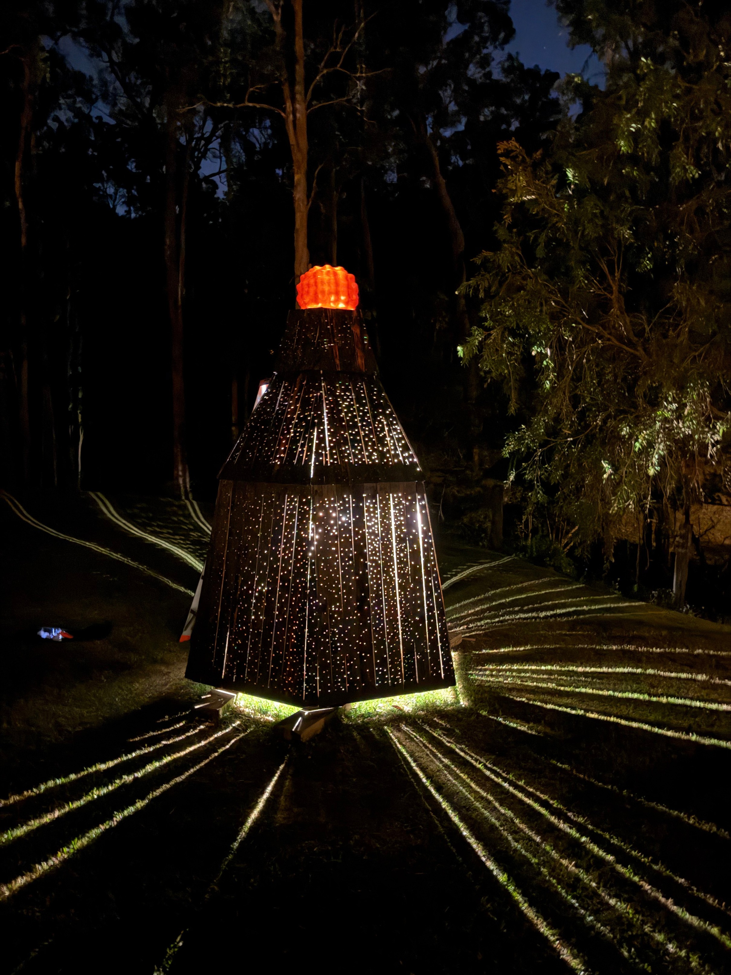 Littoral Lantern illuminated at night, casting patterned light onto the surrounding landscape